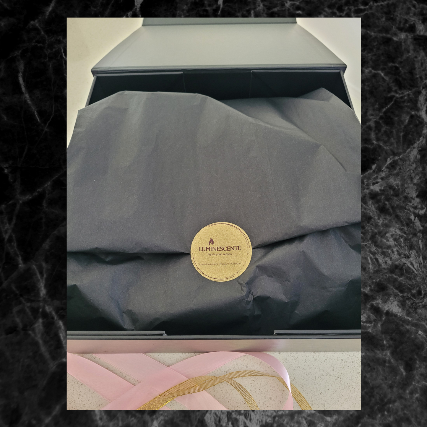 Image shows the inside of the gift hamper with black tissue paper and a gold sticker with words 'Luminescente' logo, slogan 'Ignite your senses' and 'Exquisite Artisanal Fragrance Collection'.