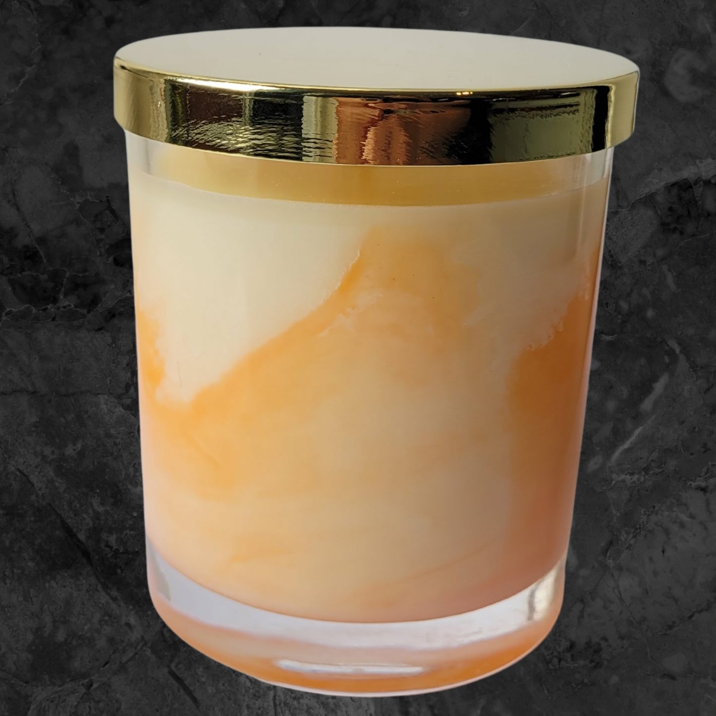 Orange and cream soy wax candle in a clear glass jar with gold lid.