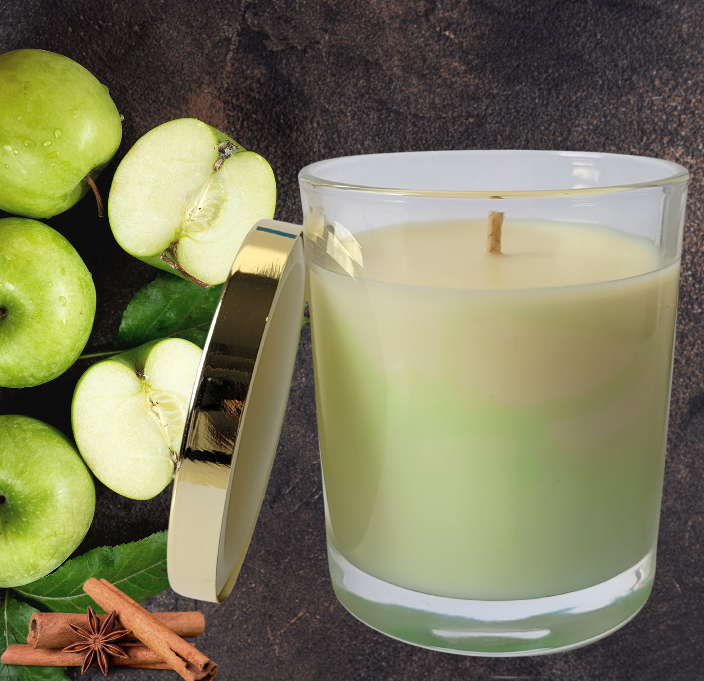 A cream and lime green marble soy wax candle in a clear glass jar with a gold lid and gold foil Luminescente logo on the front of the candle jar.
The background features green apples and cinnamon spice.