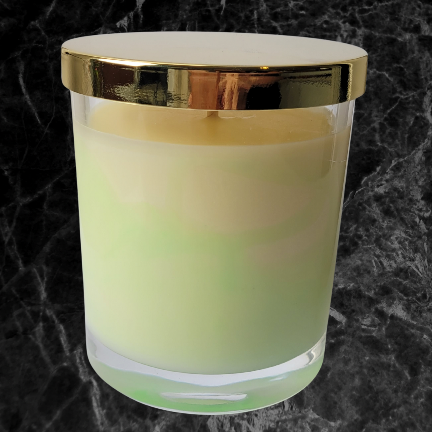A cream and lime green marbled candle in a clear glass jar with a gold lid. The front of the candle jar features a gold foil logo ‘Luminescente’.