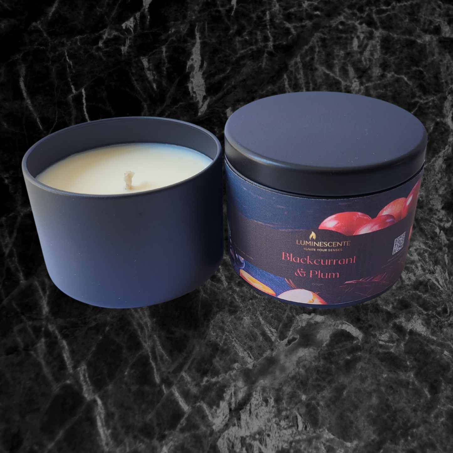 Soy candle with a single cotton wick in a black candle tin. Coloured label on tin front featuring images of blackcurrants and cut plums on a black backgeound and Luminescente logo in gold.