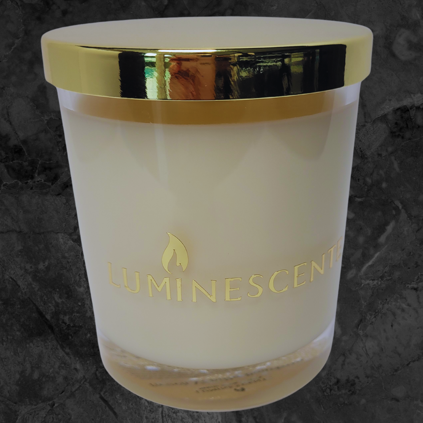 Clear glass candle jar with gold lid with a gold foil label with brand name 'Luminescente' on front.