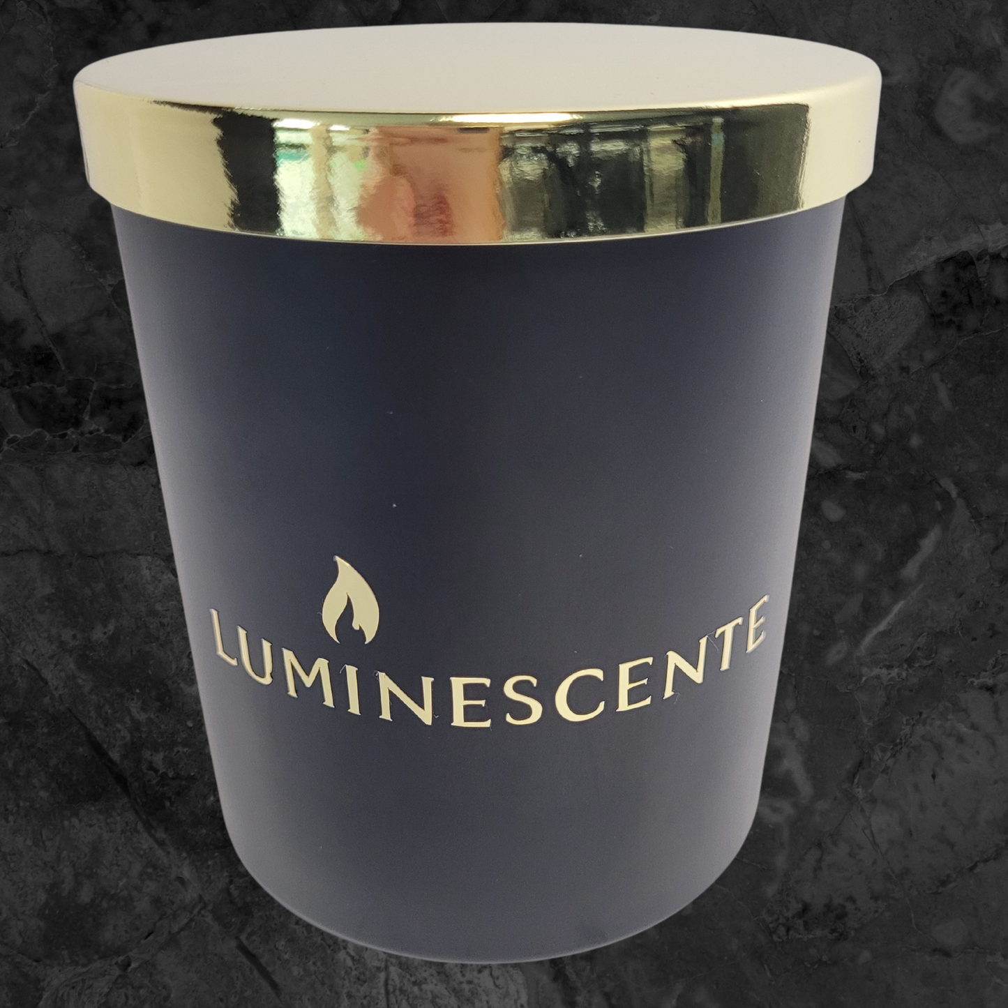 Black candle jar with gold lid with a gold foil label with brand name 'Luminescente' on front.