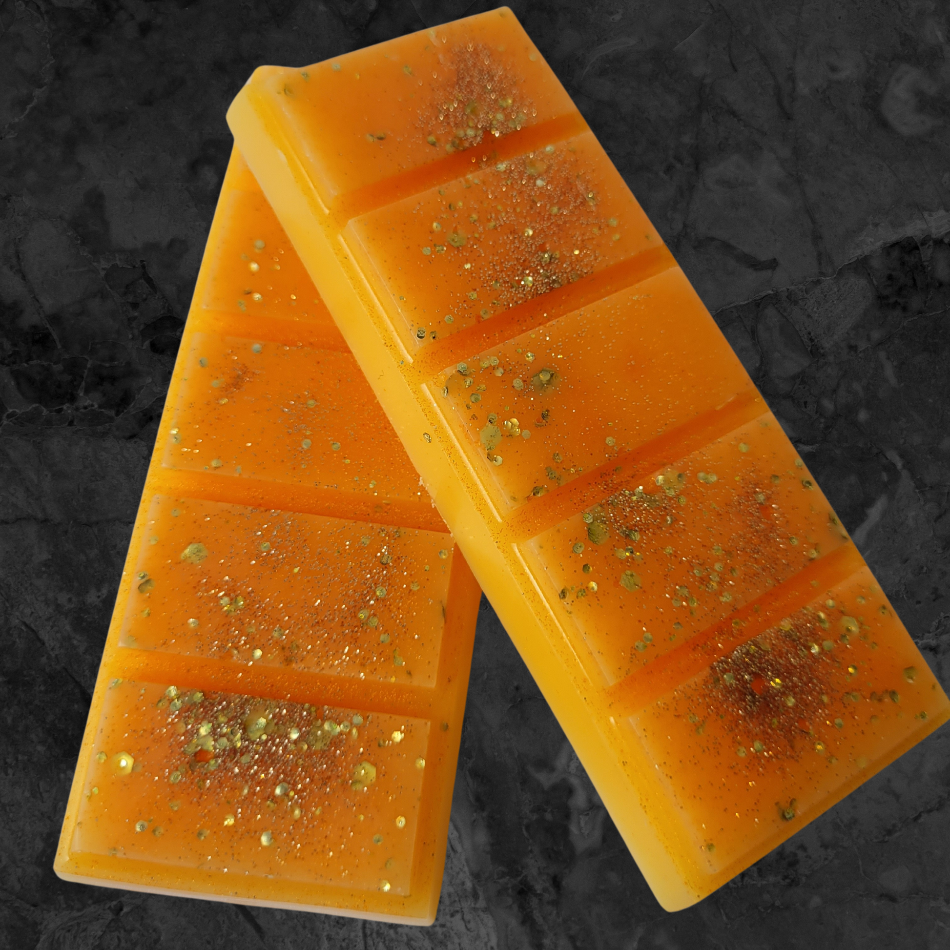 Orange soy wax snap bar melt with gold chunky and fine brown spice coloured biodegradable glitter on a black and grey background.